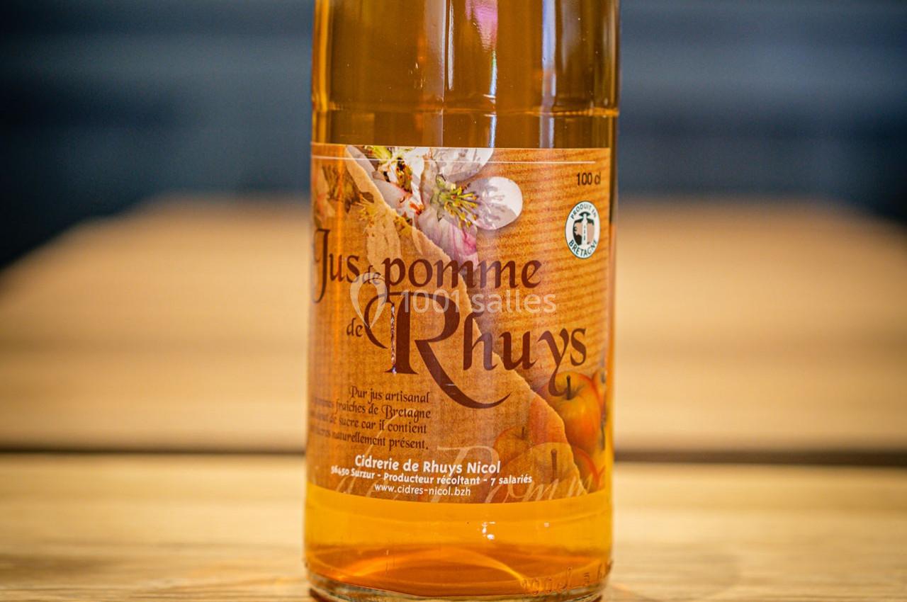 Bouteille de jus de pomme artisanal avec étiquette marron et fleur illustrée, posée sur une table en bois.
