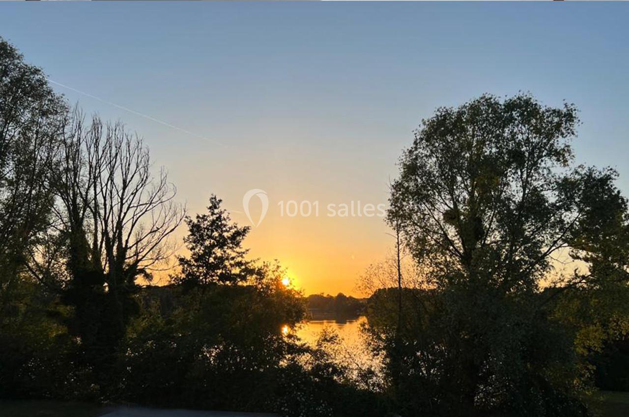 Coucher de soleil sur un lac entouré d'arbres, avec un ciel dégagé et des reflets sur l'eau.