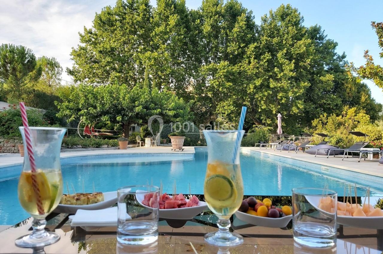 Verres de boissons fraîches et assiettes de collations disposés sur une table près d'une piscine entourée de verdure.