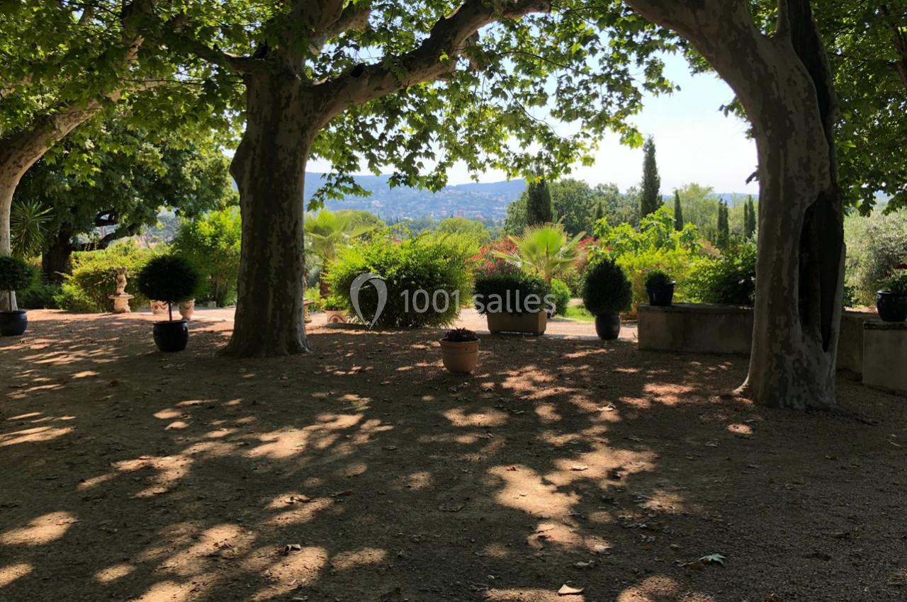 Allée ombragée bordée d'arbres et de plantes en pot, avec vue sur un paysage vallonné en arrière-plan.