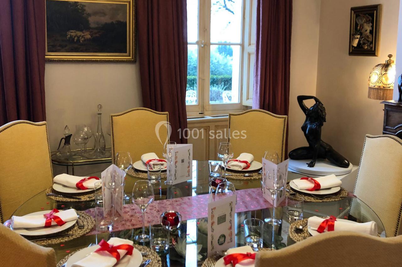 Table ronde élégamment dressée avec nappes blanches, rubans rouges, et décorations dans une salle à manger lumineuse.