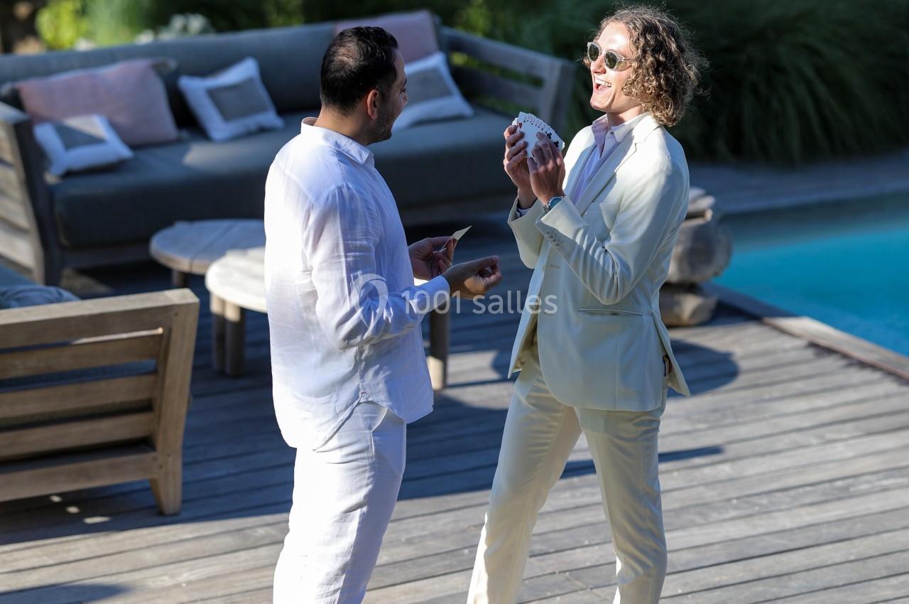 Deux hommes discutent sur une terrasse en bois près d'une piscine, entourés de mobilier extérieur.
