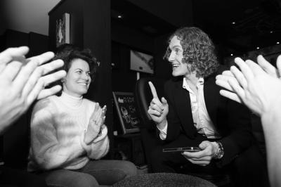 Miniature Robin Geyer - Magicien Professionnel Français #5 Un homme en costume parle avec animation à une femme souriante dans un café, entourés de mains applaudissant.