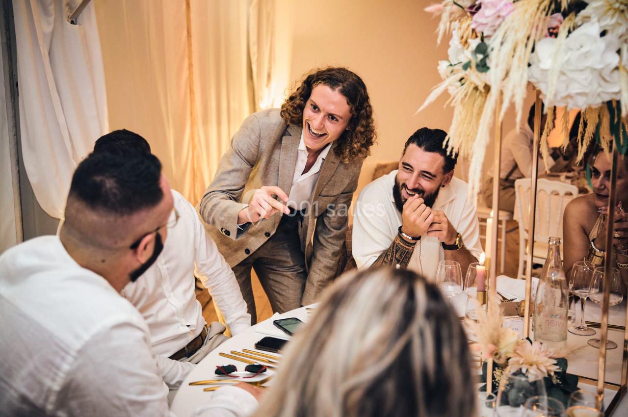 Un homme en costume amuse des convives assis autour d'une table décorée lors d'un événement festif.