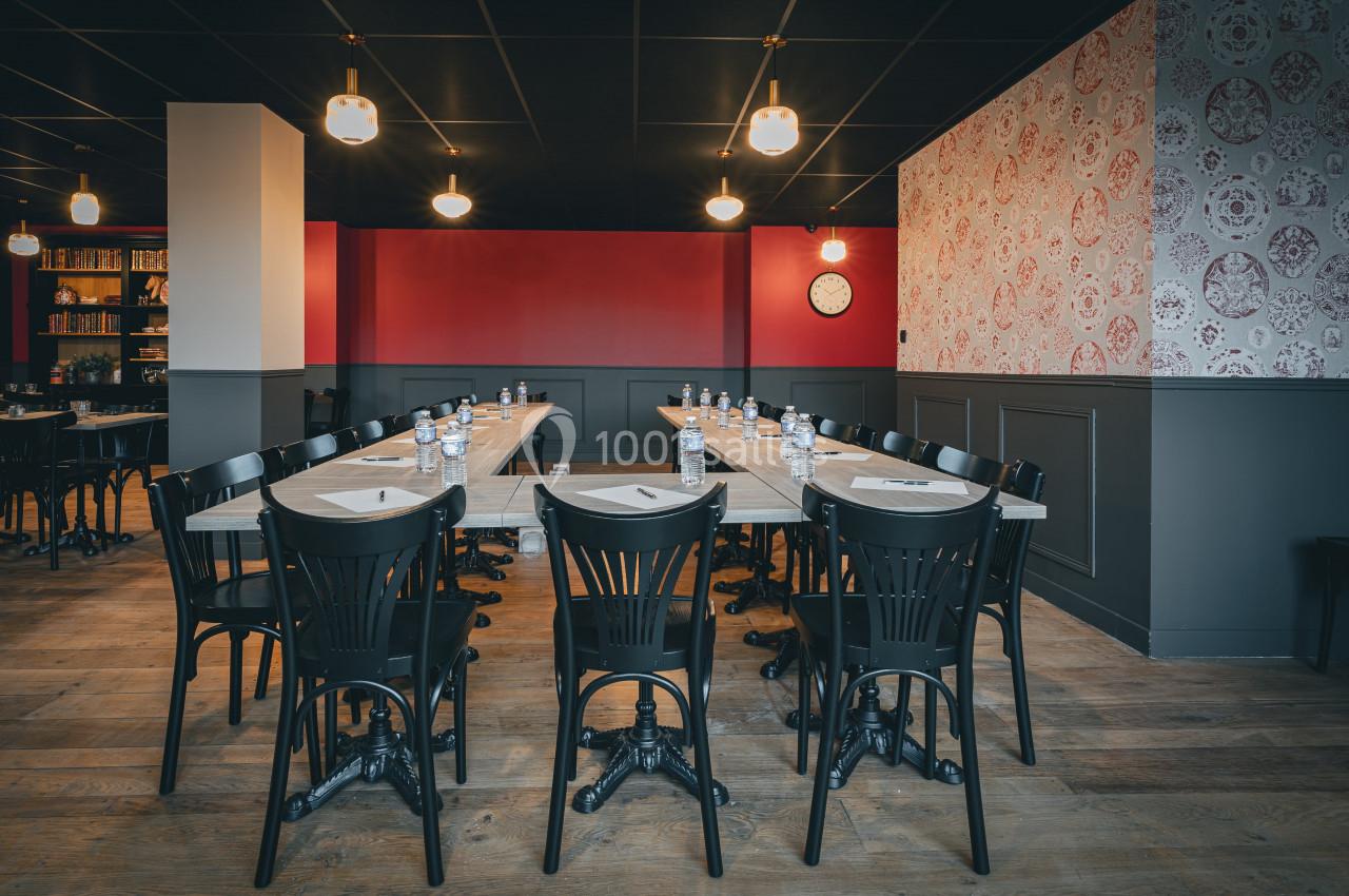 Salle de réunion avec tables en U, chaises noires, bouteilles d'eau et carnets, éclairée par des suspensions.