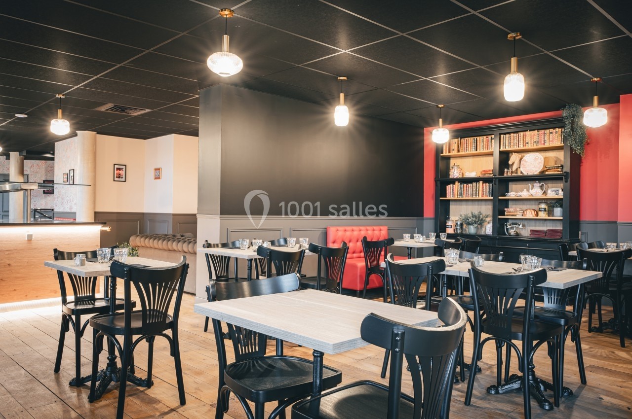 Salle de restaurant lumineuse avec tables en bois, chaises noires, étagère décorative et banquette rouge.