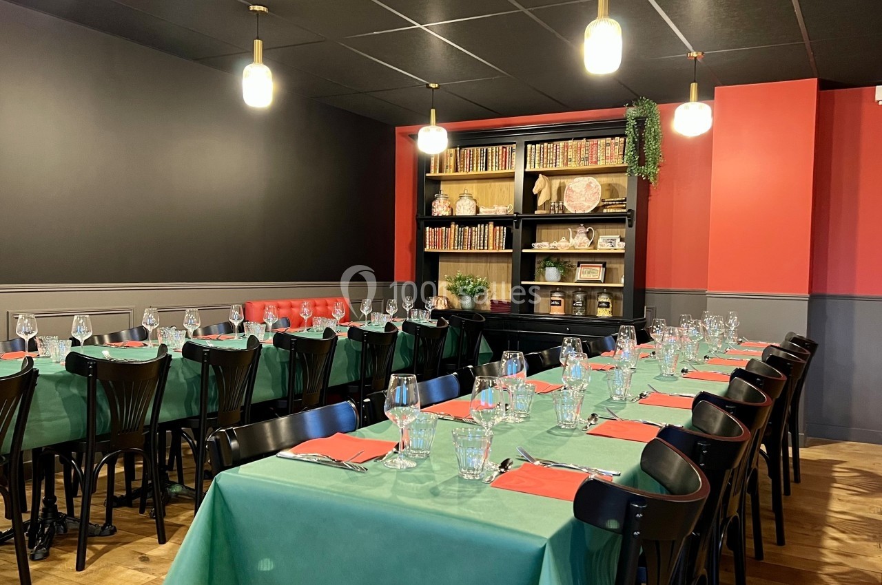 Salle de restaurant avec tables alignées, nappes vertes, serviettes rouges, chaises noires et étagères décoratives en…