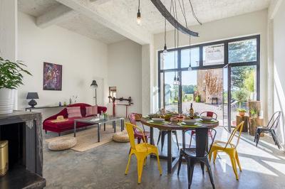 Chambre lumineuse avec lit double, fauteuil beige, fenêtre ouverte sur un paysage et décoration murale en osier.