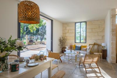 Chambre lumineuse avec lit double, fauteuil beige, fenêtre ouverte sur un paysage et décoration murale en osier.