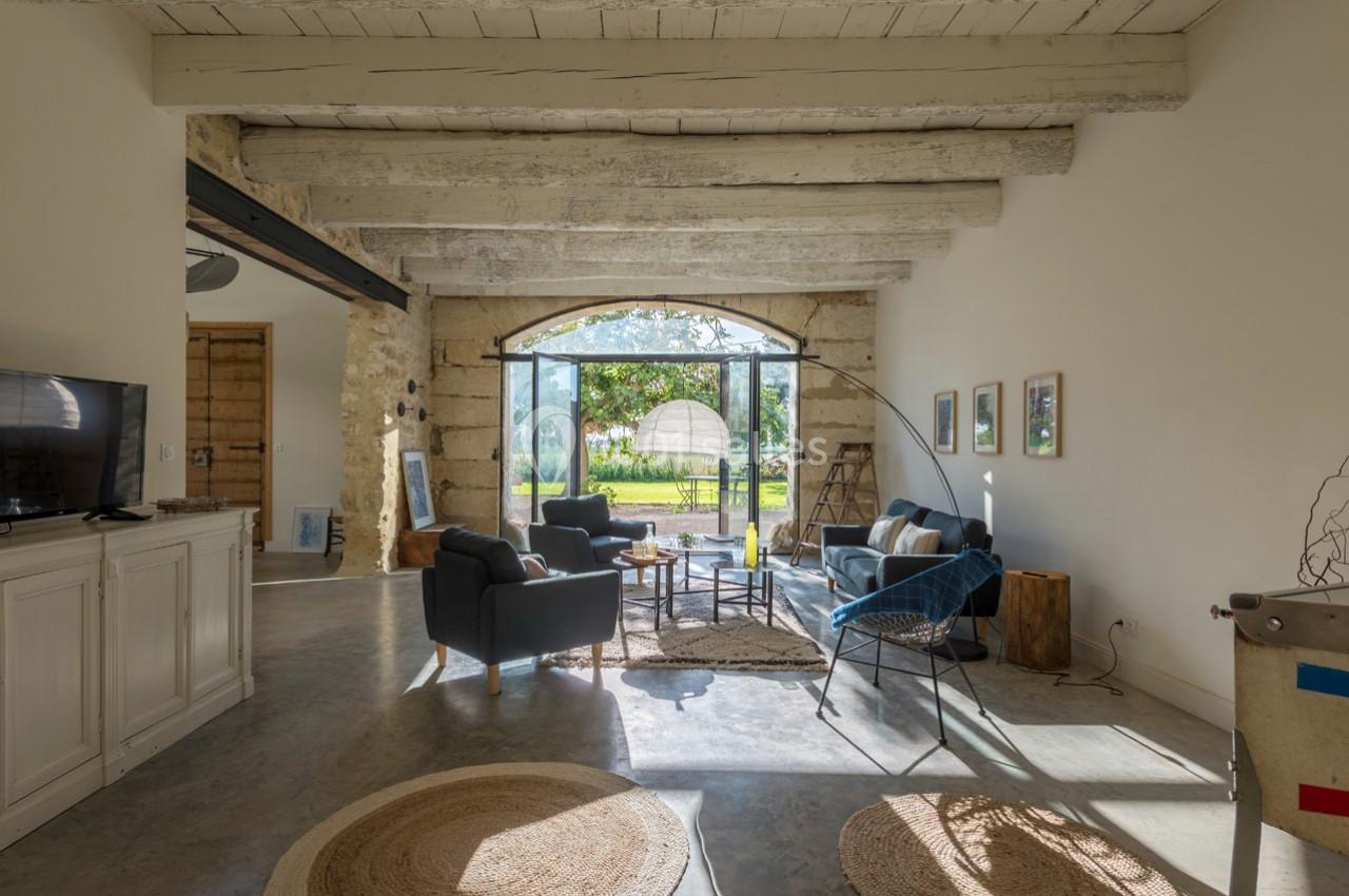 Salon lumineux avec poutres apparentes, mobilier contemporain, grande baie vitrée donnant sur un jardin verdoyant.