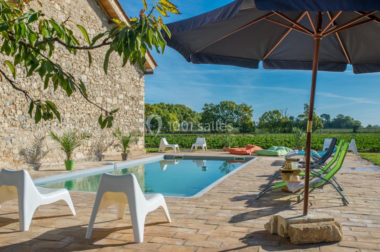 Piscine extérieure entourée de chaises et parasols, située près d'une maison en pierre avec vue sur la campagne.