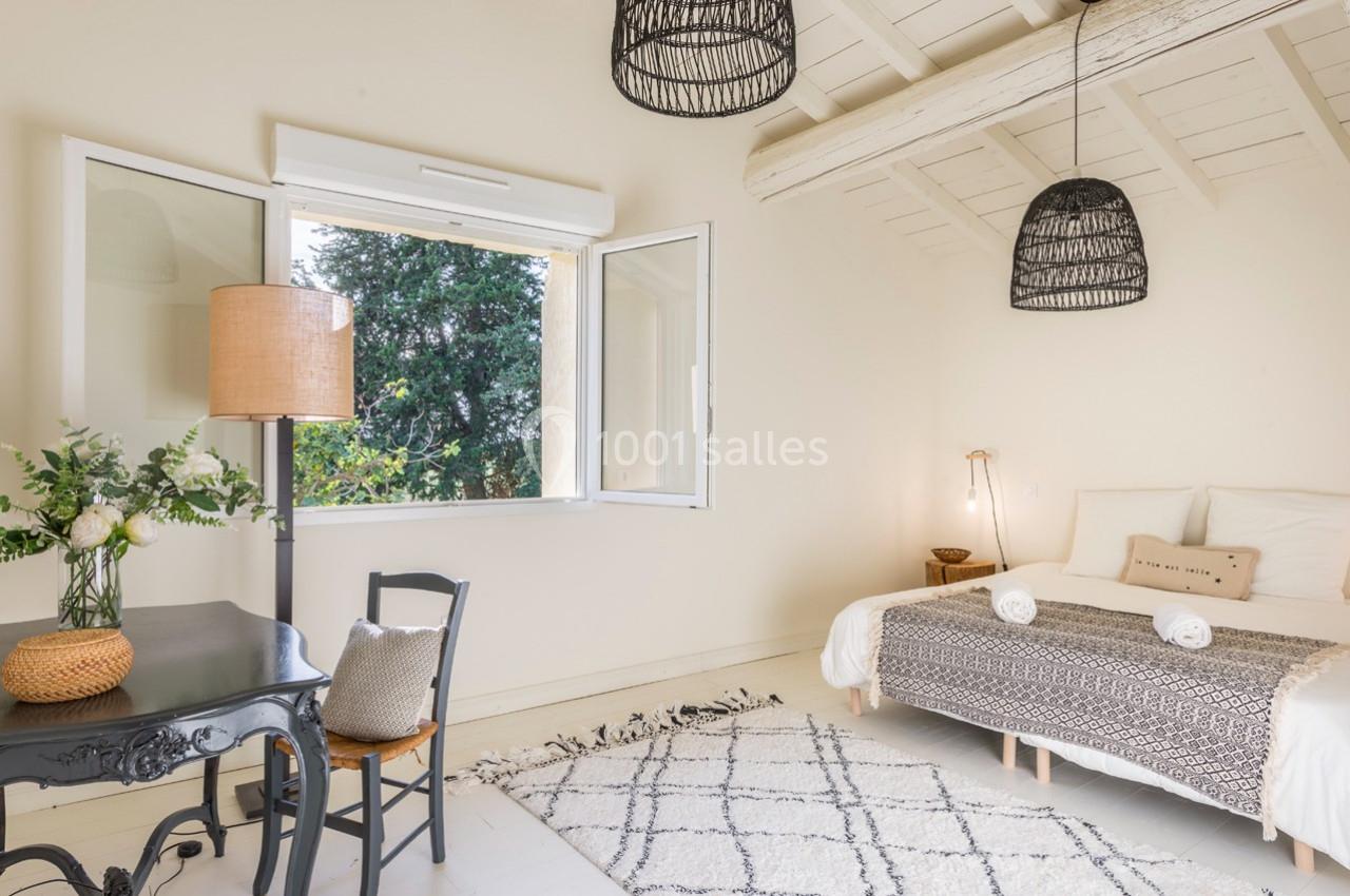 Chambre lumineuse avec lit double, bureau noir, lampe en rotin et fenêtre ouverte donnant sur un arbre.