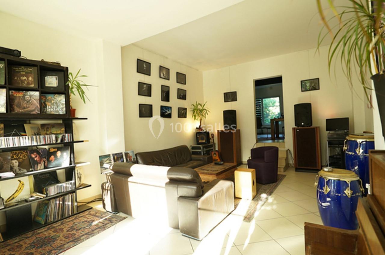 Salon lumineux avec étagères de disques, instruments de musique, fauteuils et enceintes audio.