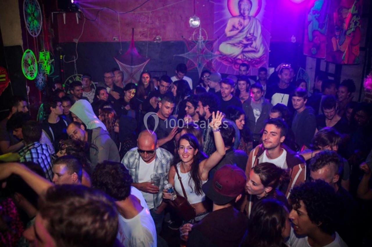 Groupe de personnes dans une ambiance festive, éclairée par des lumières colorées, avec des décorations murales visibles.