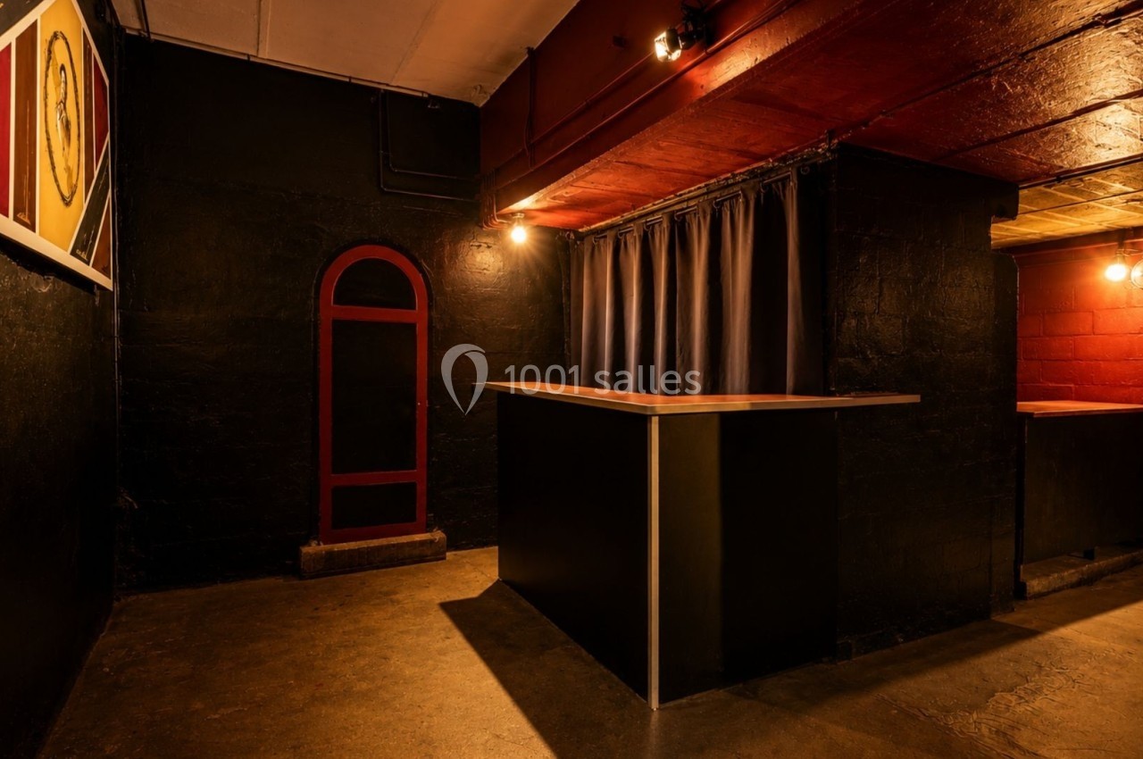 Espace intérieur sombre avec murs noirs et rouges, comptoirs modernes et éclairage tamisé.