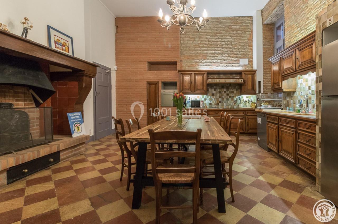 Cuisine spacieuse avec grande table en bois, cheminée en briques, meubles rustiques et carrelage à motifs.