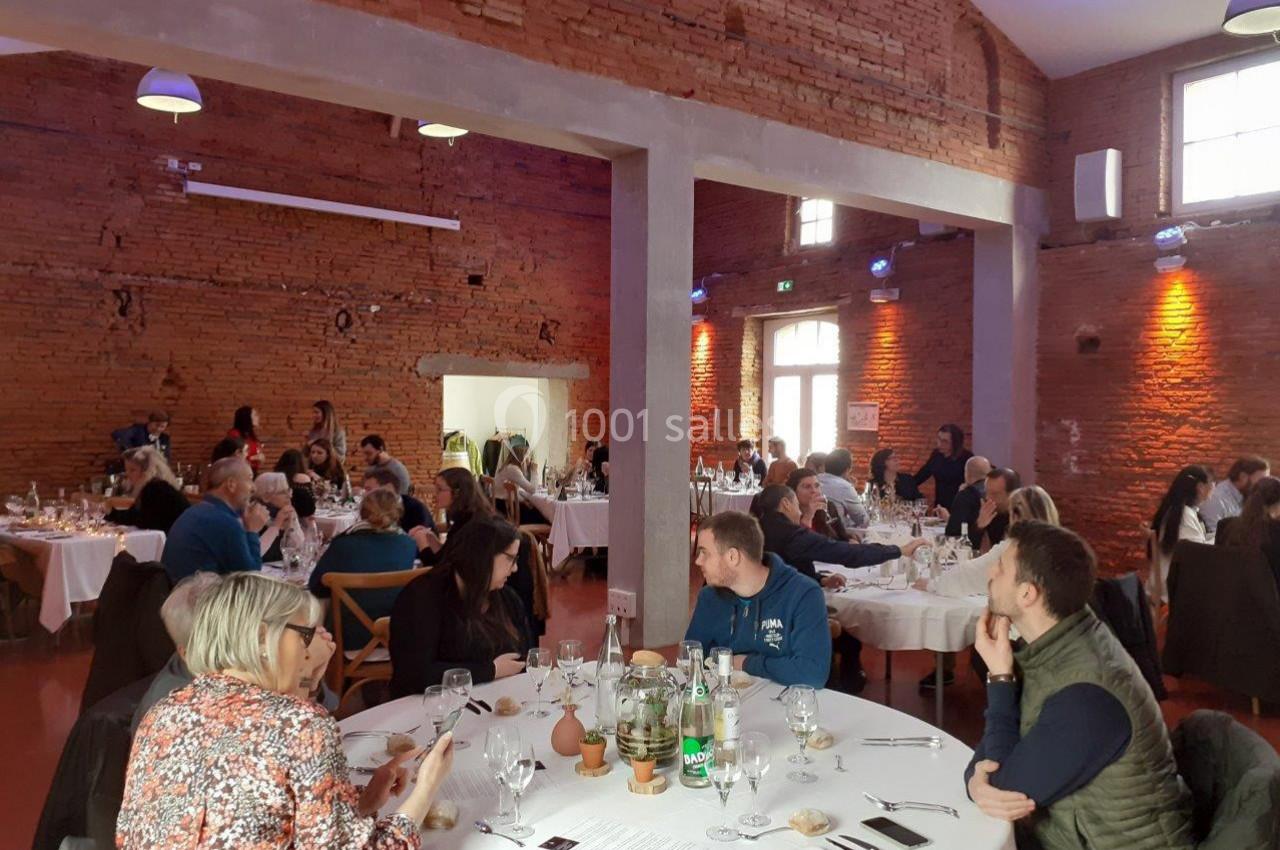 Salle en briques rouges avec des convives assis autour de tables rondes, partageant un repas dans une ambiance conviviale.