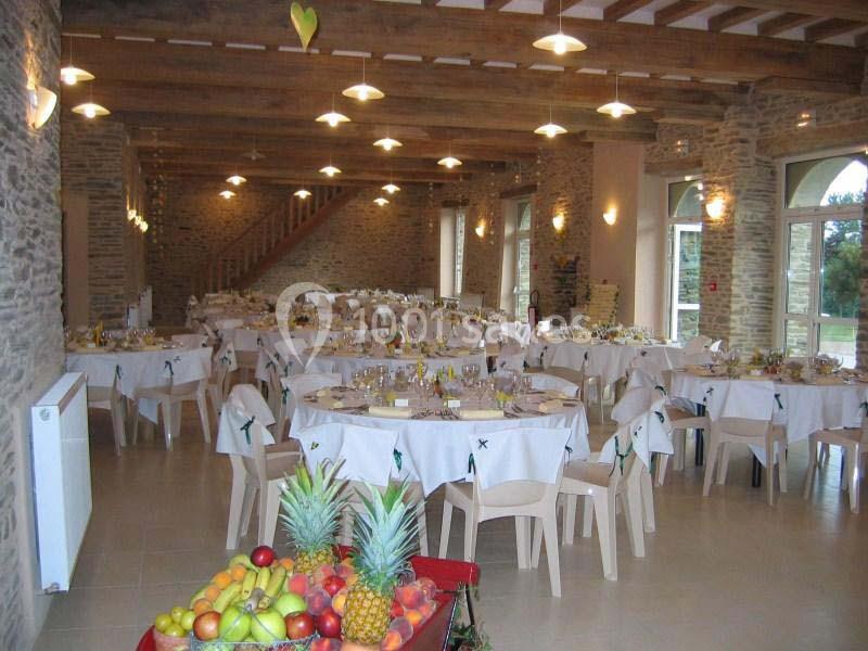 Salle de réception décorée avec des tables rondes dressées et un buffet de fruits au premier plan.