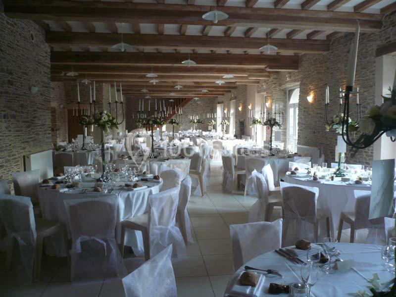 Salle de réception élégamment décorée avec des tables rondes dressées, nappes blanches et chandeliers.