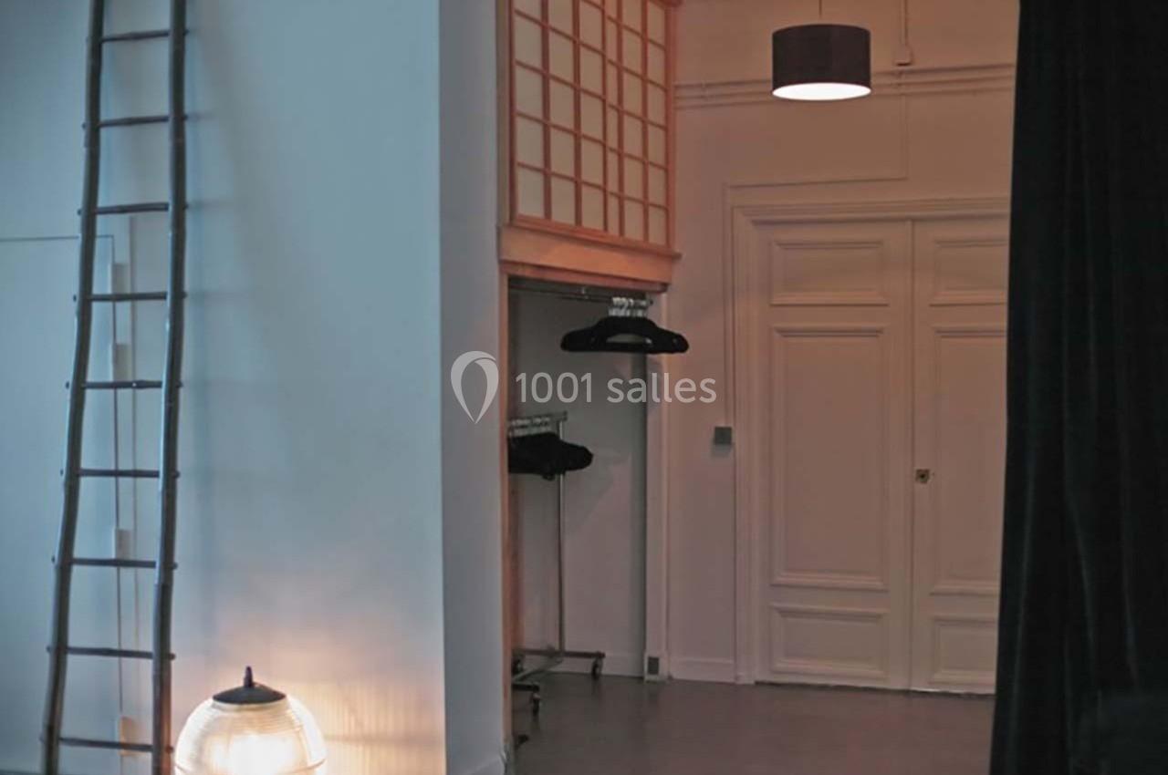 Intérieur avec une échelle, un portant à vêtements, une porte blanche et un éclairage tamisé.