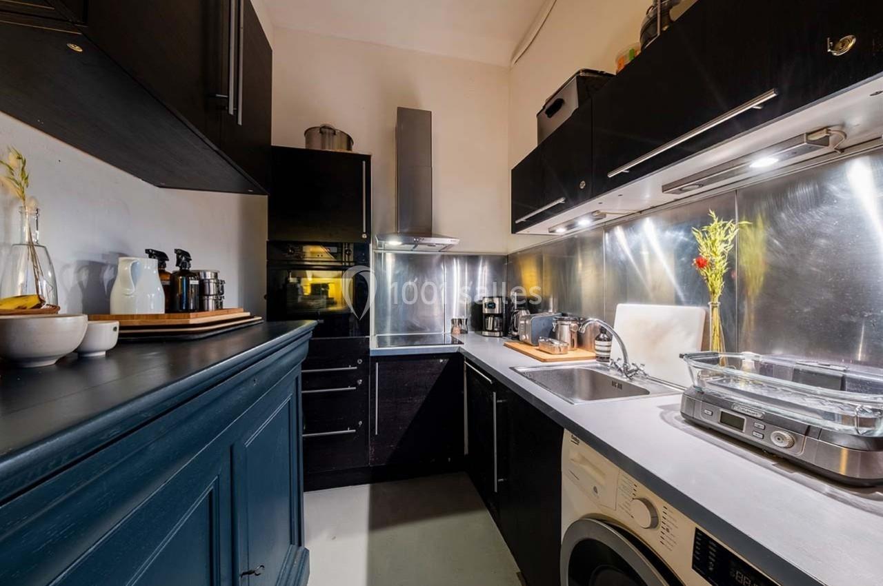 Cuisine moderne avec meubles noirs, plan de travail en acier inoxydable, électroménagers et éclairage intégré.