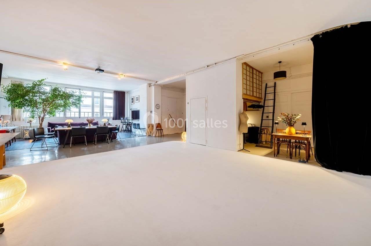 Grand espace lumineux avec coin salon, table à manger, mezzanine accessible par une échelle et décoration minimaliste.