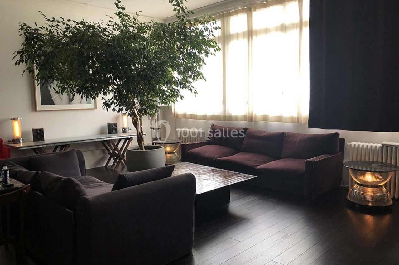 Salon lumineux avec parquet sombre, canapés en tissu, grande plante d'intérieur et table basse en bois.