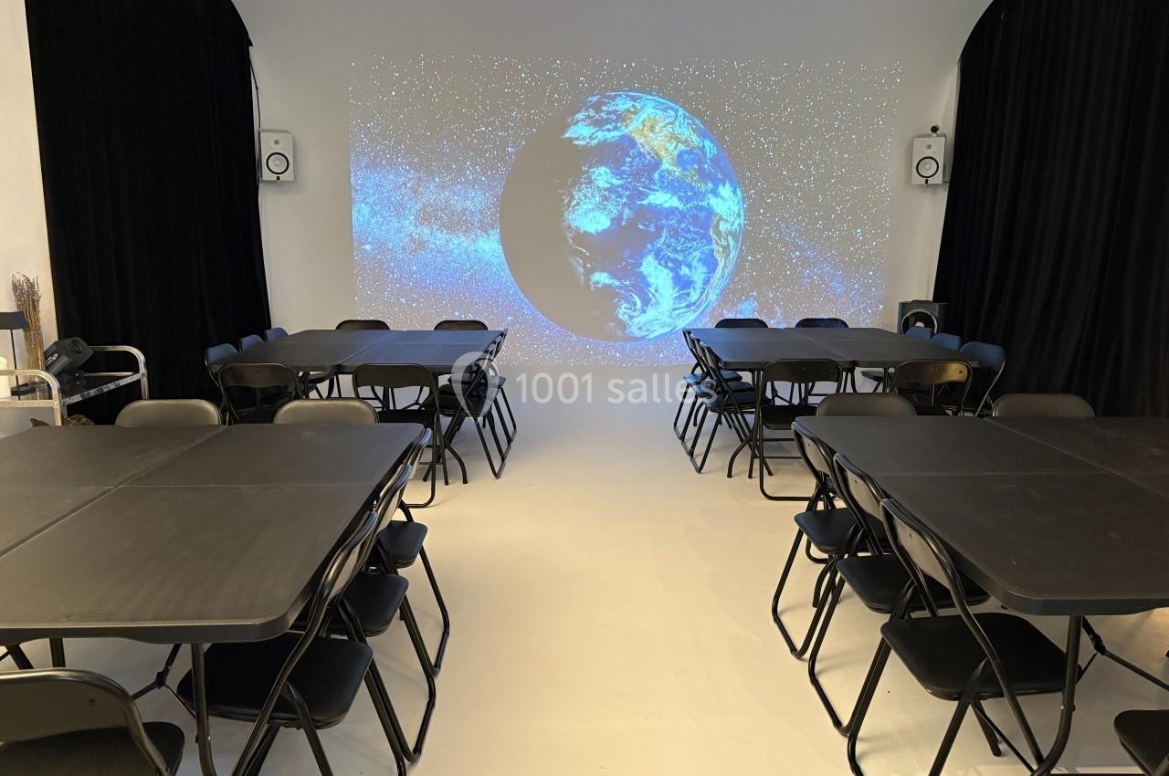 Salle équipée de tables et chaises noires, avec une projection de la Terre sur un mur blanc entouré de rideaux noirs.