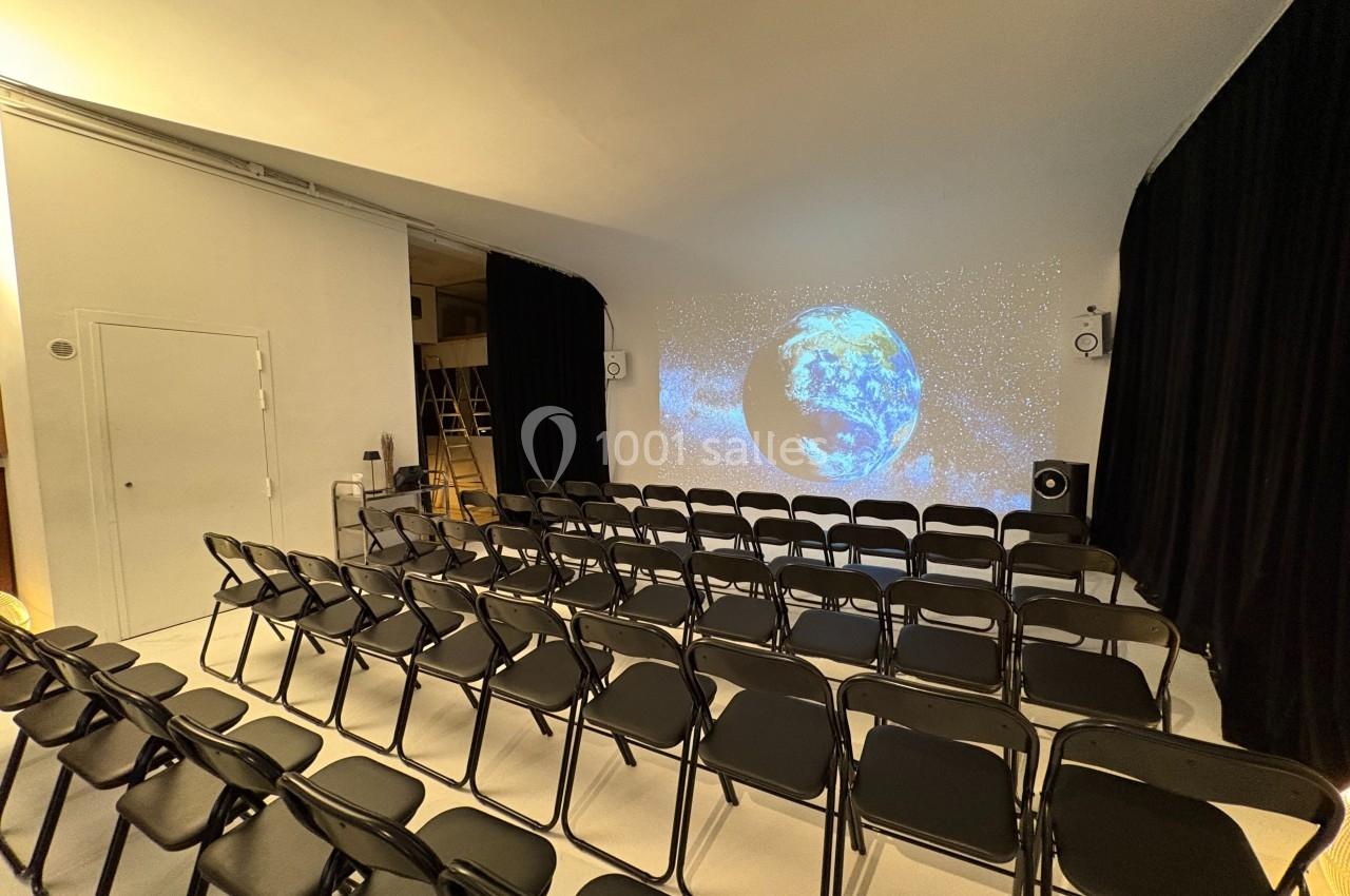 Salle avec des rangées de chaises noires face à un écran projetant une image de la Terre dans l'espace.