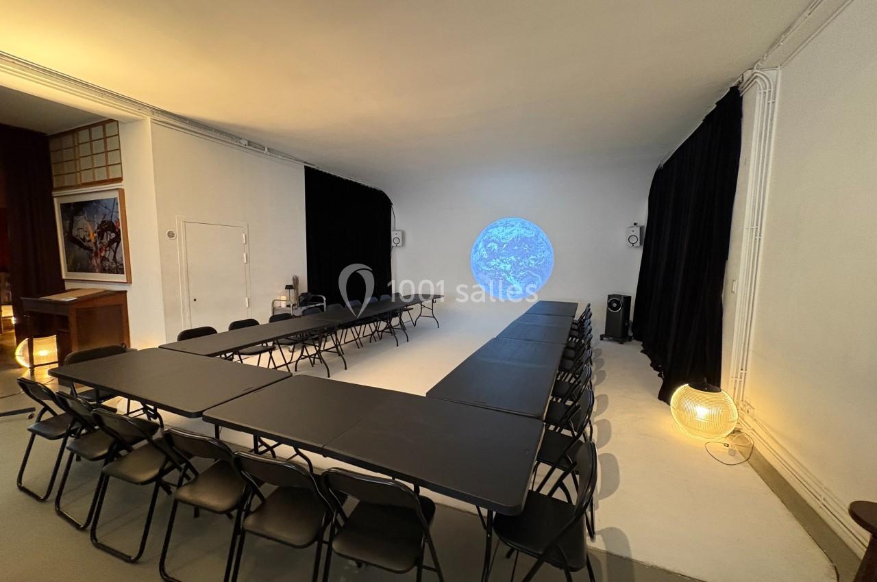 Salle de réunion avec tables en U, chaises noires, éclairage doux et projection d'une image de la Terre au mur.