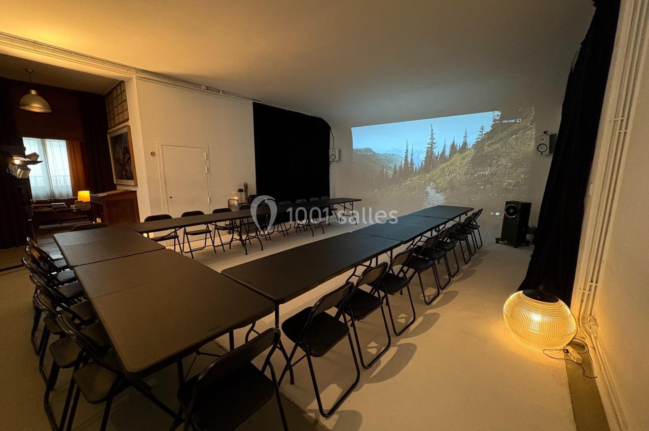 Salle de réunion avec tables disposées en U, chaises noires et projection d'un paysage naturel sur un mur.