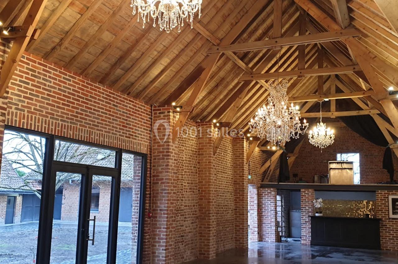Location salle Haverskerque (Nord) - Ferme d'Hercule #4 Intérieur d'une salle avec murs en briques, charpente en bois apparente et lustres suspendus.