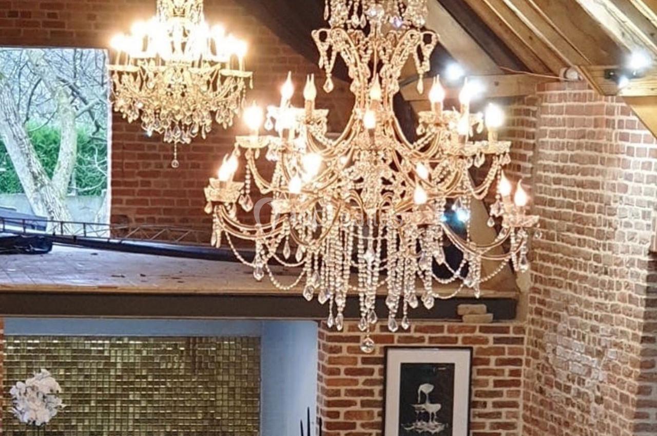 Location salle Haverskerque (Nord) - Ferme d'Hercule #9 Deux lustres en cristal suspendus dans une pièce aux murs en briques, avec une grande fenêtre et un plafond en bois.