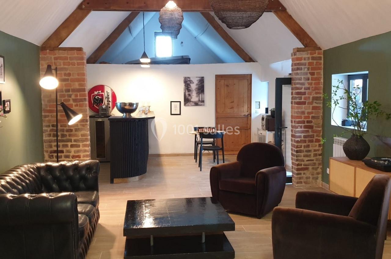 Location salle Haverskerque (Nord) - Ferme d'Hercule #18 Salon chaleureux avec murs en briques et verts, mobilier en cuir et bois, éclairage doux et décoration moderne.