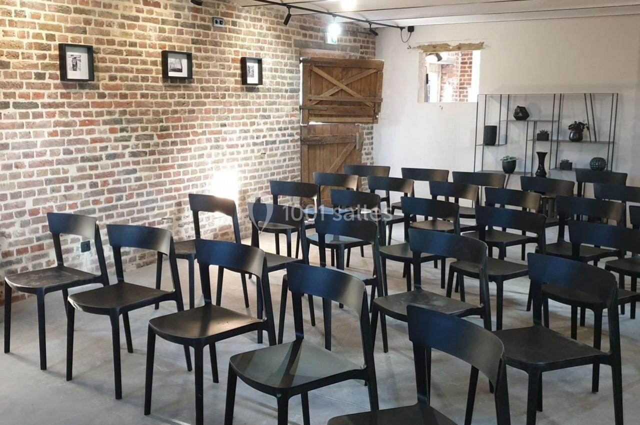 Location salle Haverskerque (Nord) - Ferme d'Hercule #15 Salle avec des chaises noires alignées, murs en briques, porte en bois et étagères décoratives en arrière-plan.