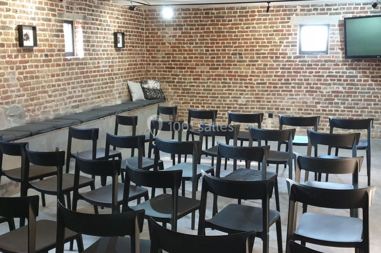 Location salle Haverskerque (Nord) - Ferme d'Hercule #17 Salle avec des murs en briques, rangées de chaises noires alignées et un écran fixé au mur.