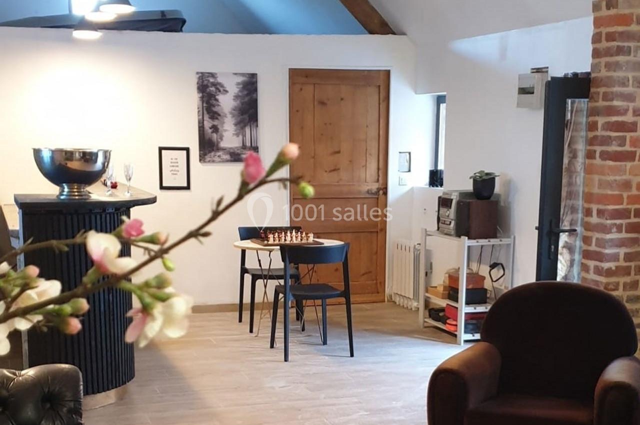 Location salle Haverskerque (Nord) - Ferme d'Hercule #19 Salle lumineuse avec mobilier moderne, table avec échiquier, mur en briques et décoration minimaliste.