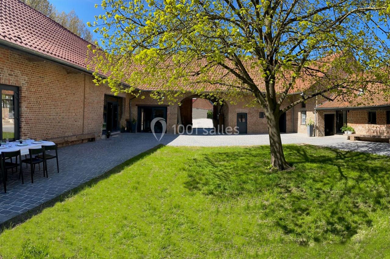 Location salle Haverskerque (Nord) - Ferme d'Hercule #25 Cour intérieure d'une ferme rénovée en briques, avec un arbre au centre et des tables dressées sur la gauche.