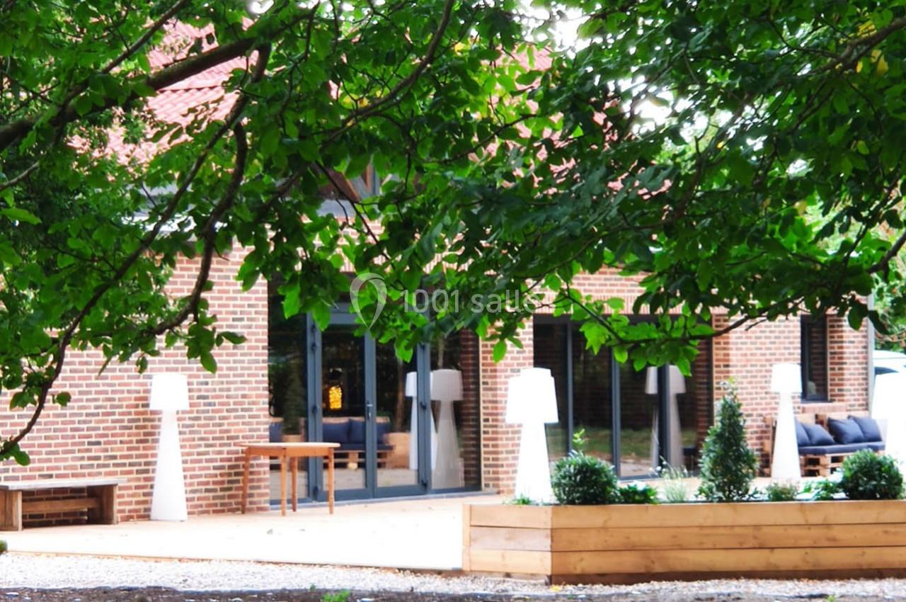 Location salle Haverskerque (Nord) - Ferme d'Hercule #6 Façade en briques d'une maison avec terrasse aménagée, entourée de verdure et de jardinières en bois.