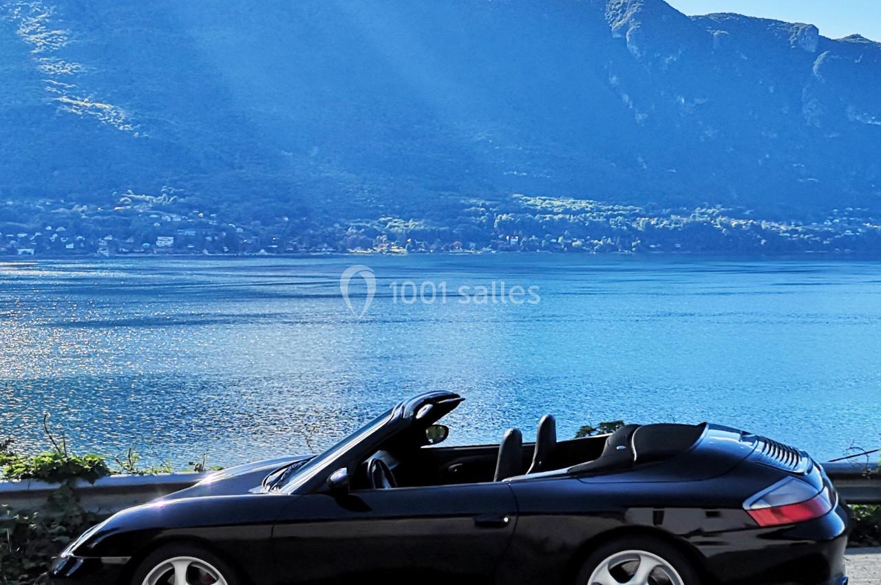 Photo David J. Location #14 Voiture décapotable noire garée près d'un lac, avec des montagnes et un ciel bleu en arrière-plan.