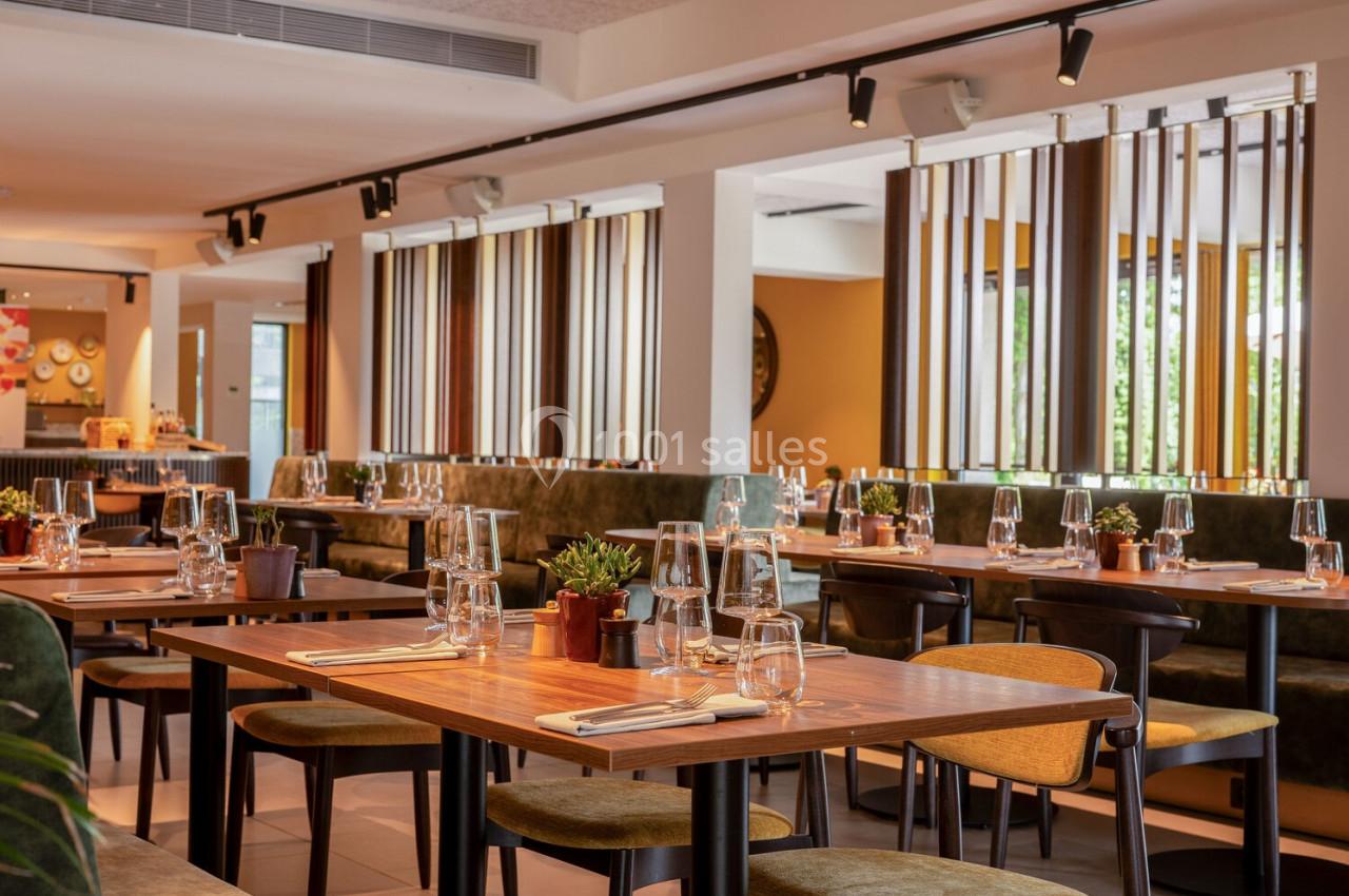 Salle de restaurant lumineuse avec tables en bois dressées, chaises modernes et décoration végétale.