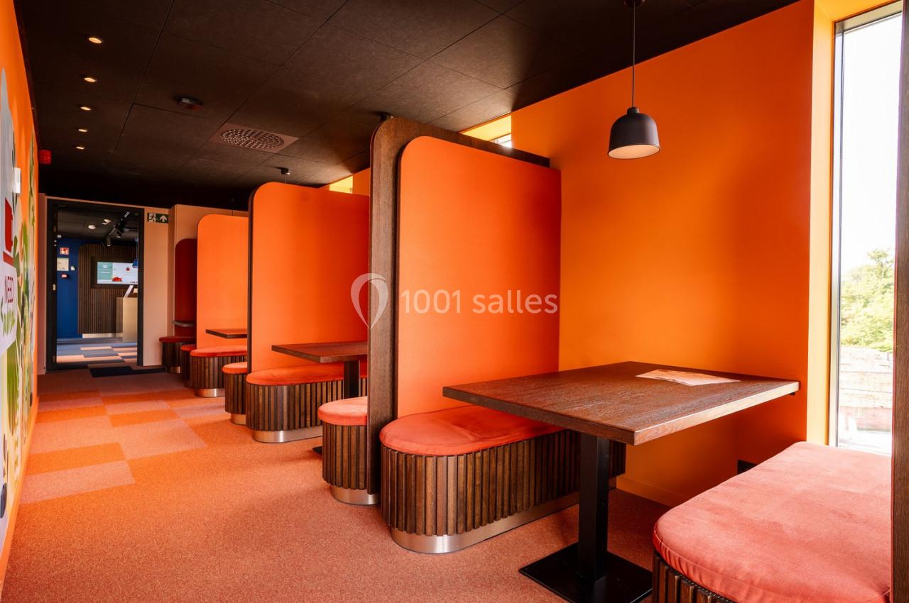 Banquettes en bois et orange avec tables assorties dans un espace lumineux au design moderne et coloré.