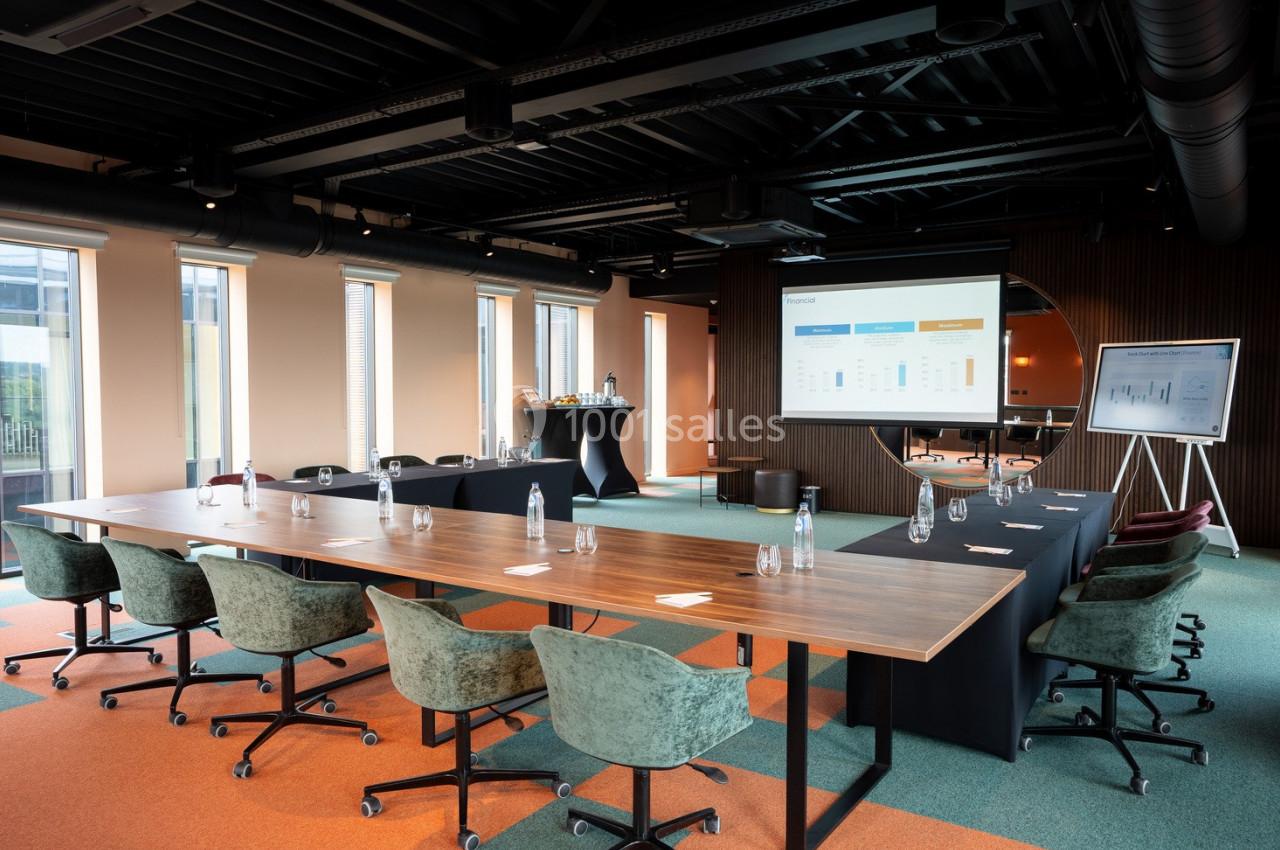 Salle de réunion moderne avec grande table, chaises, écran de présentation, tableau blanc et lumière naturelle.