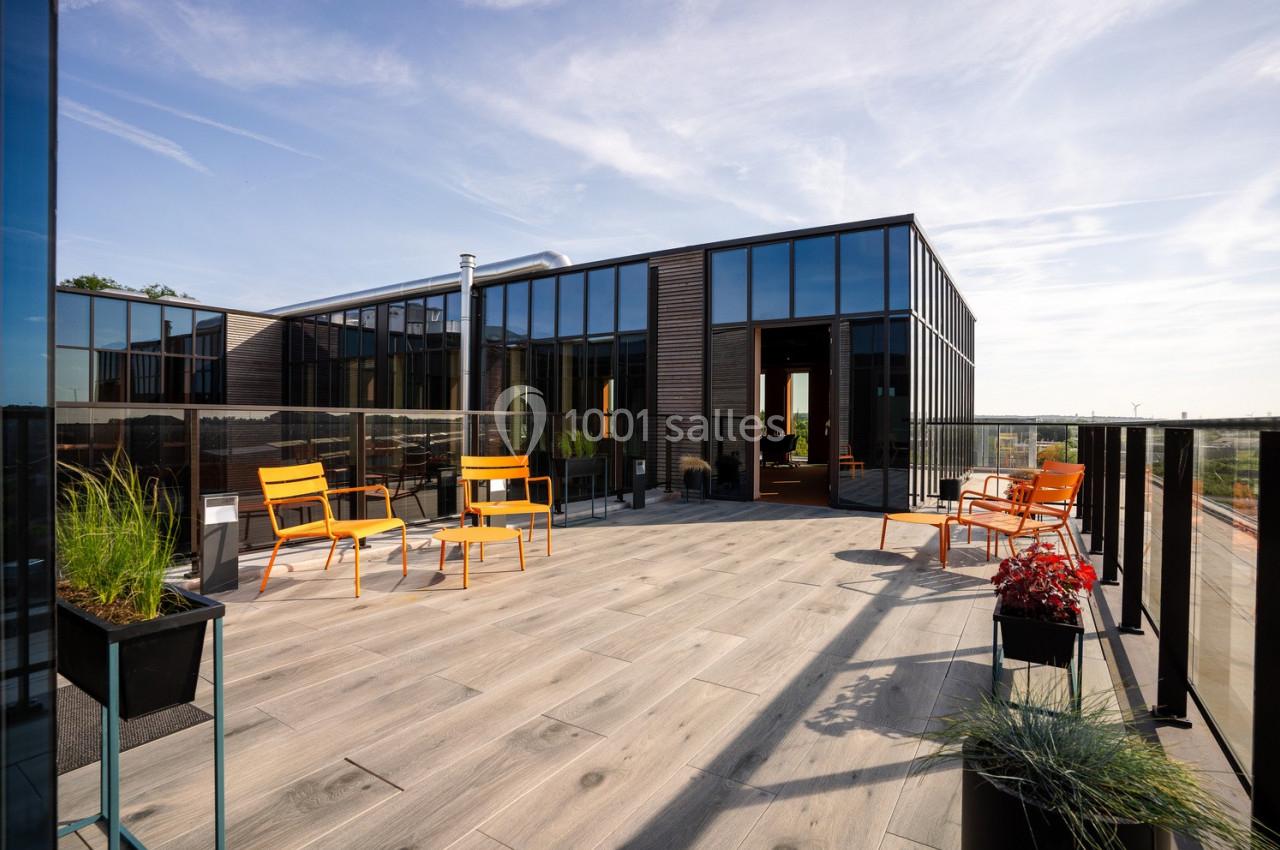 Terrasse spacieuse avec mobilier orange, entourée de baies vitrées et de plantes, sous un ciel dégagé.