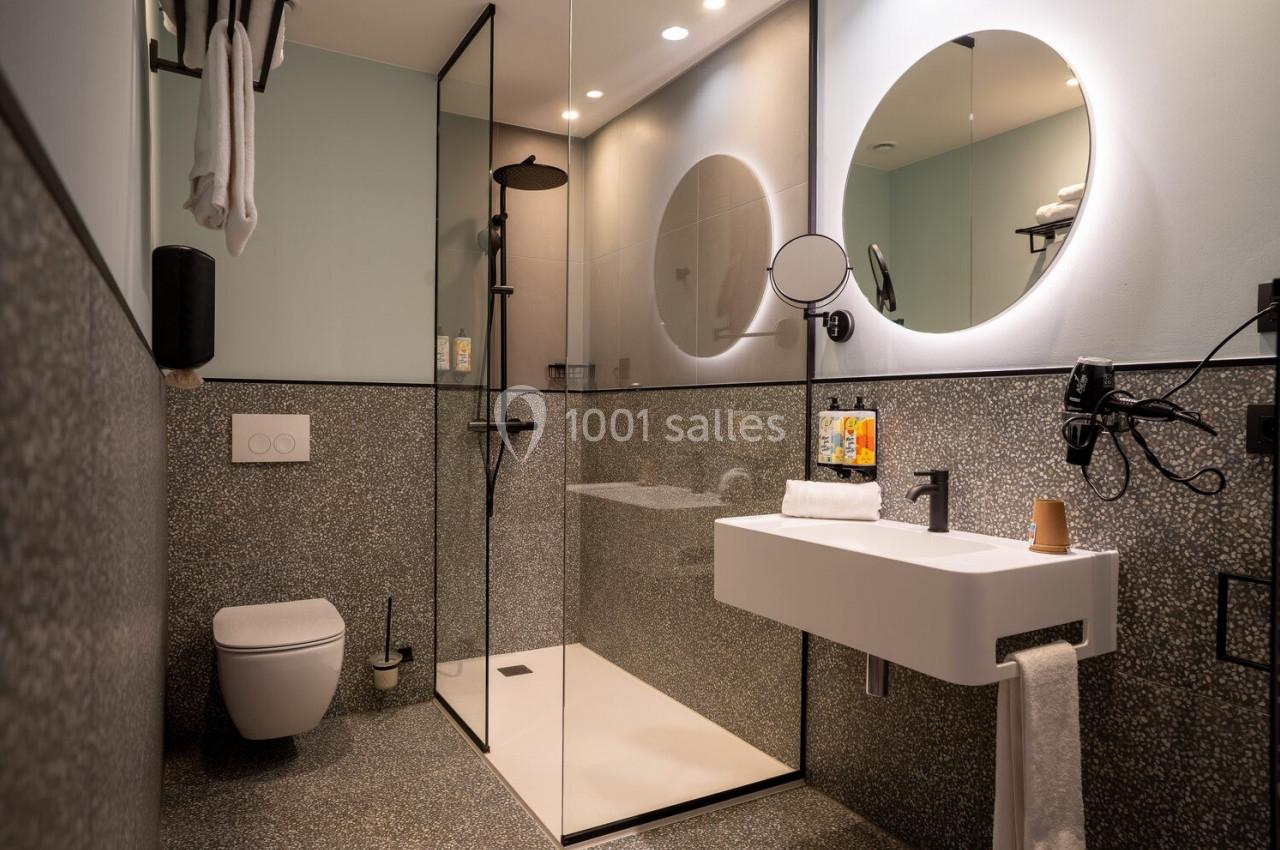 Salle de bain moderne avec douche à l'italienne, lavabo suspendu, miroir rond et toilettes suspendues.