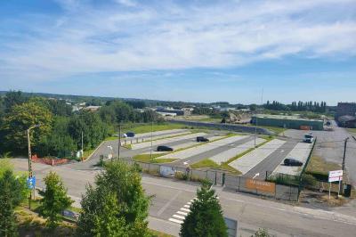 Vue aérienne d'un parking vide entouré de végétation, avec quelques voitures stationnées et un ciel dégagé.