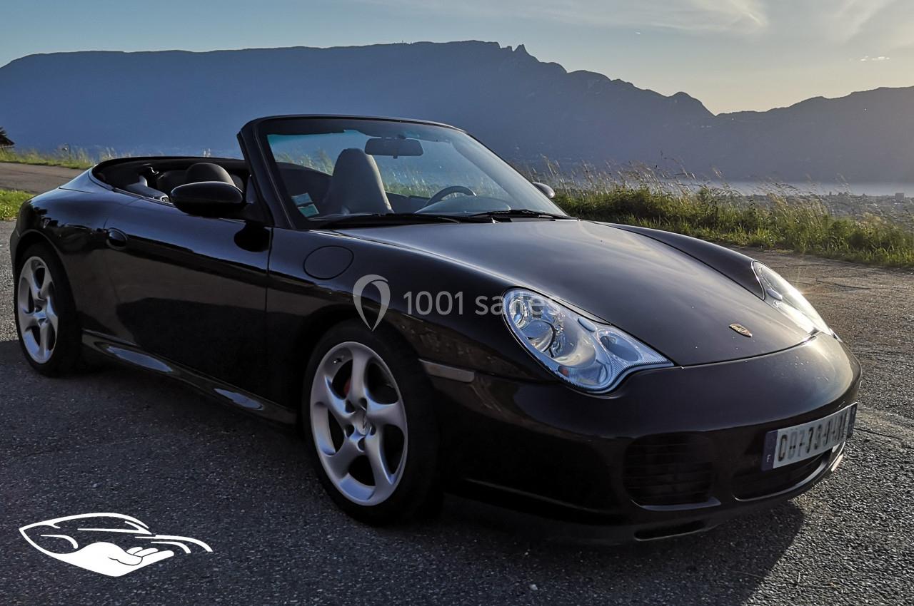 Voiture décapotable noire stationnée sur une route, avec une montagne en arrière-plan sous un ciel clair.