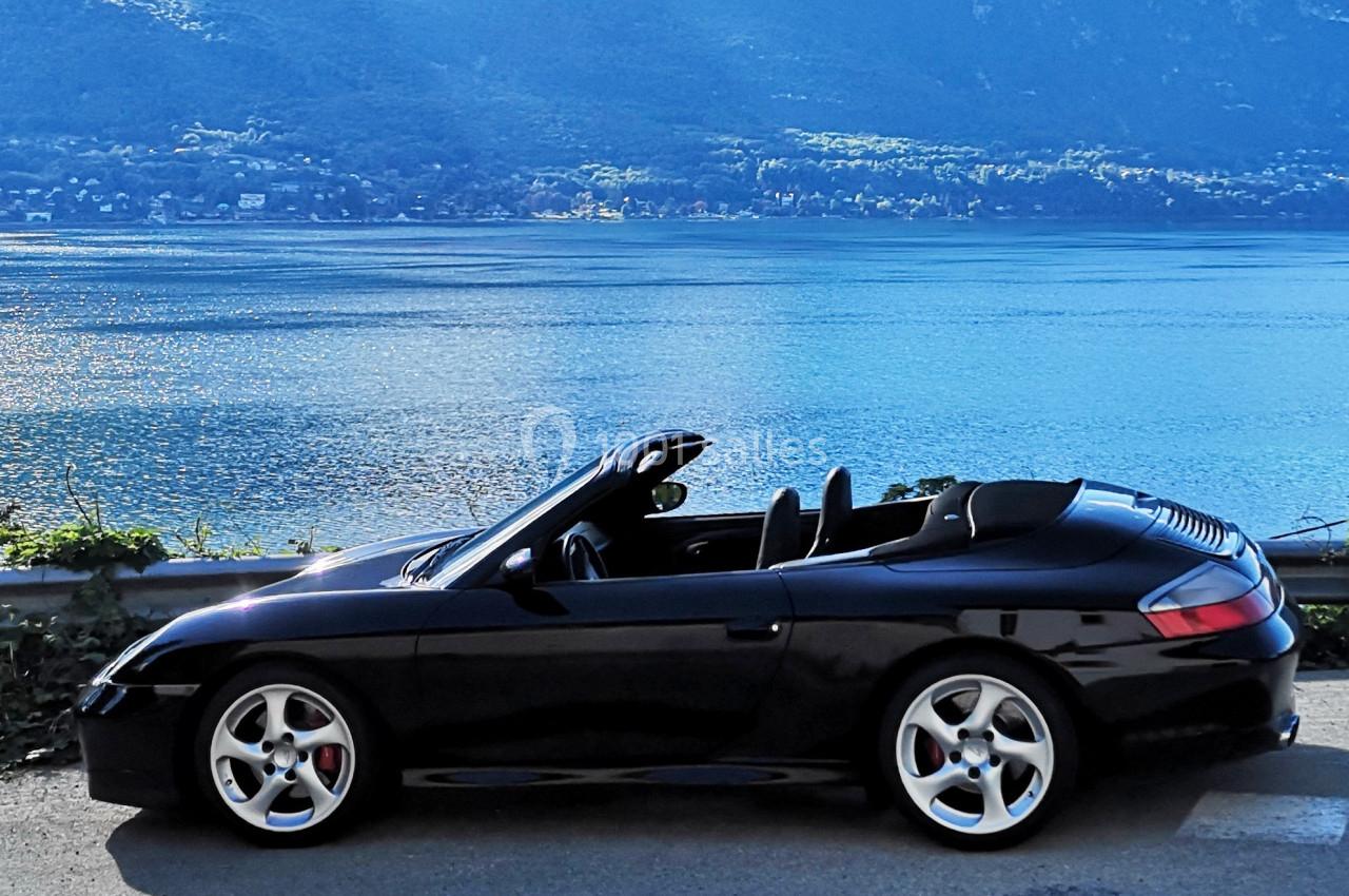 Voiture décapotable noire garée près d'un lac avec des collines en arrière-plan.