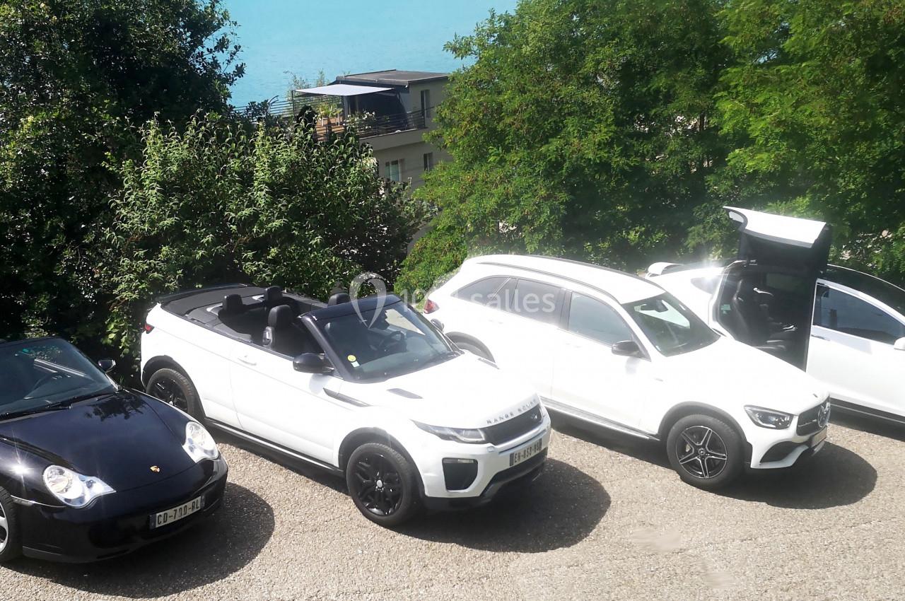 Quatre voitures, dont deux décapotables noires et blanches, stationnées sur un parking près d'un lac et de végétation.