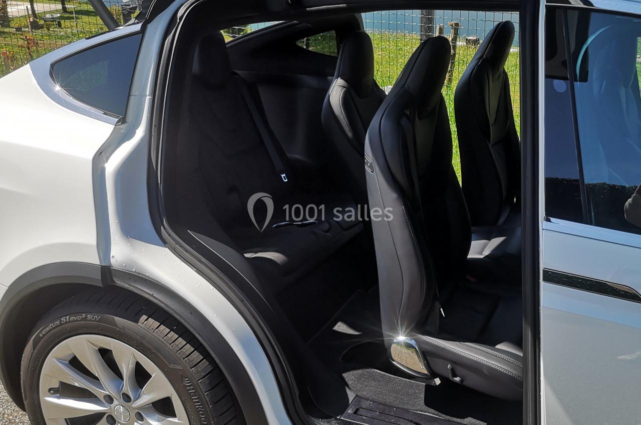 Portière arrière ouverte d'une voiture montrant deux rangées de sièges noirs en cuir et un intérieur spacieux.